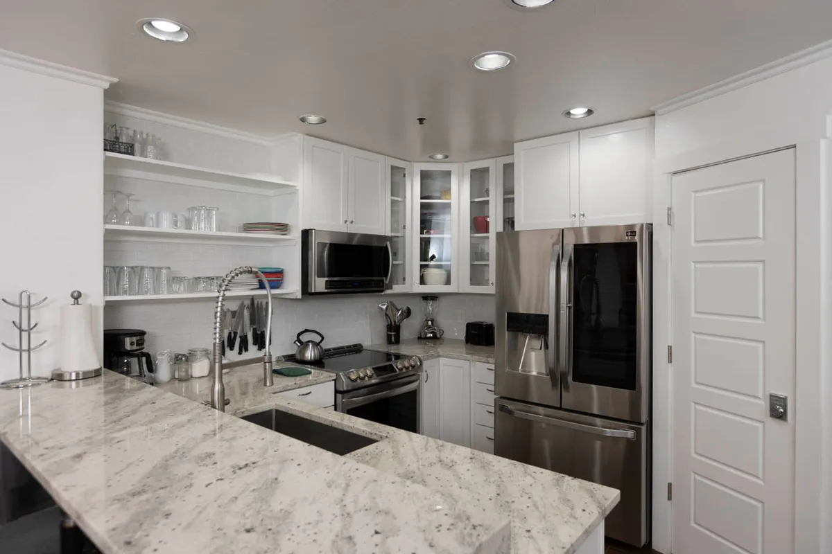 A modern kitchen with granite countertops, stainless steel appliances, and open shelving. The space is bright and inviting, designed for both cooking and socializing, making it easy for guests to prepare meals or entertain visitors between work sessions.